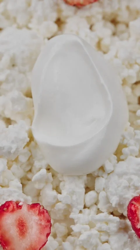 Vertical close-up of fresh cottage cheese topped with a spoonful of sour cream Stock Footage 318475641
