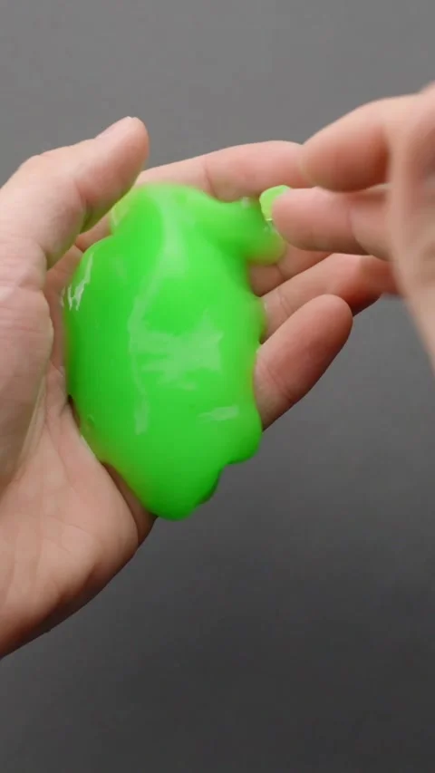 Vertical close-up of green slime toy being squeezed in hand for ASMR and stress Stock Footage 314252869