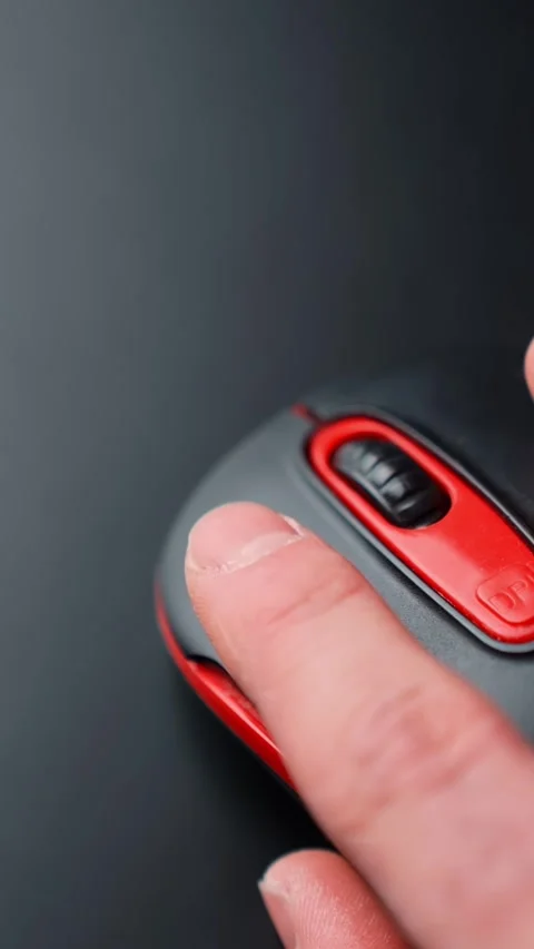 Vertical close-up of a hand clicking a red and black computer mouse on dark Stock Footage 329002456