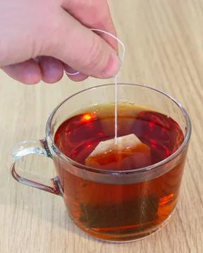 Vertical close-up of hand dipping tea bag into glass cup with hot tea Foto stock