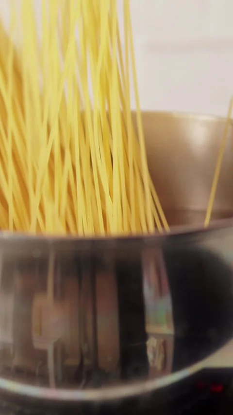 Vertical close up of a hand dropping a bundle of raw yellow spaghetti into a Stock Footage 345206228