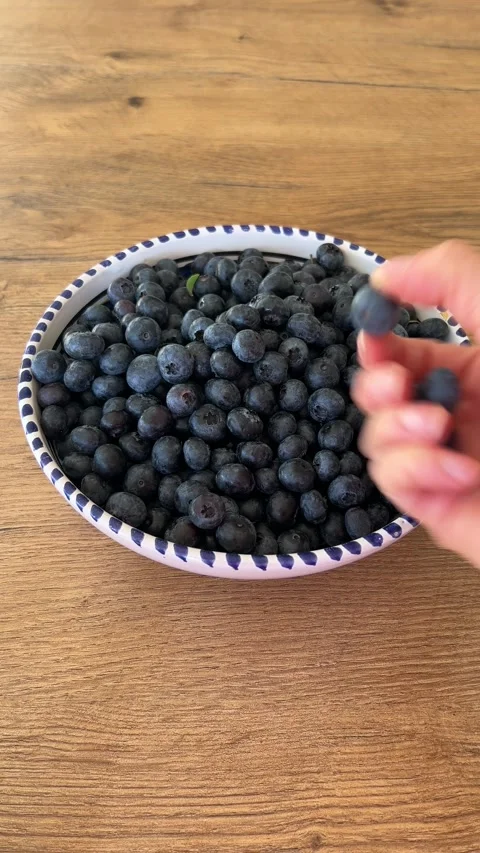 Vertical close up of hand taking fresh blueberries from bowl and showing them Video stock 346494318