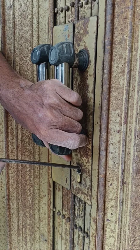 Vertical close-up of a hand unlocking a rusty iron folding door with a key a Vidéo 342965292