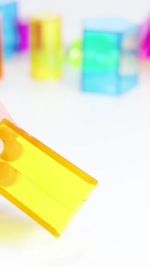 Vertical Close-Up of Hands Manipulating a Yellow Translucent Geometric Prism Stock Footage 327346675