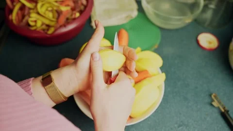 Vertical close-up of hands slicing peeled potato with a paring knife over a Video stock 328950299