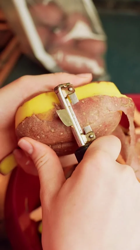 Vertical close-up of hands using a peeler to remove skin from a potato over a Vídeo Stock 331487469