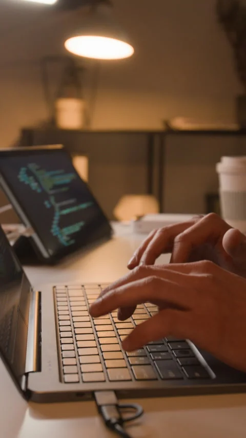 Vertical Close-up of Man Coding on Laptop with Tablet Displaying Code at Night Stock Footage 336710395