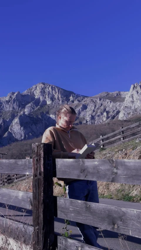 Vertical close up of man reading book in front of dramatic mountain scenery Video stock 336623181