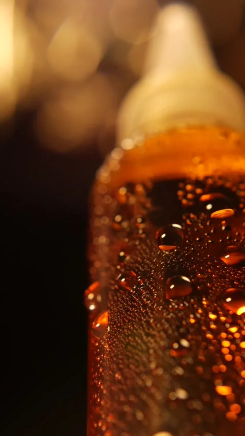 Vertical close-up of a moist glass bottle with golden liquid, its shiny surface Stock Footage 314888979