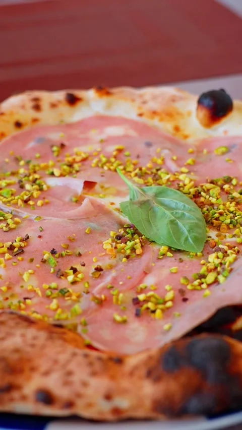Vertical close-up of mortadella and pistachio pizza with basil on a blistered Stock Footage 334729006