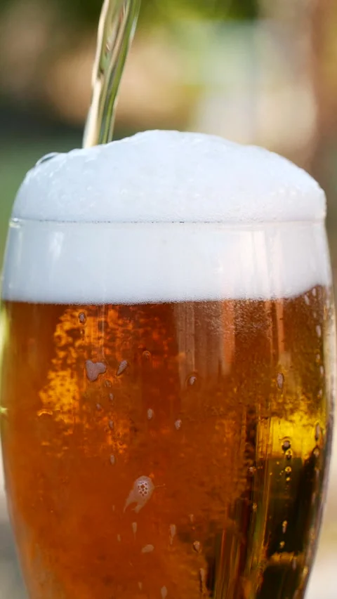 Vertical close-up of pouring beer with foam and bubbles in glass in slow motion Stock Footage 276153222