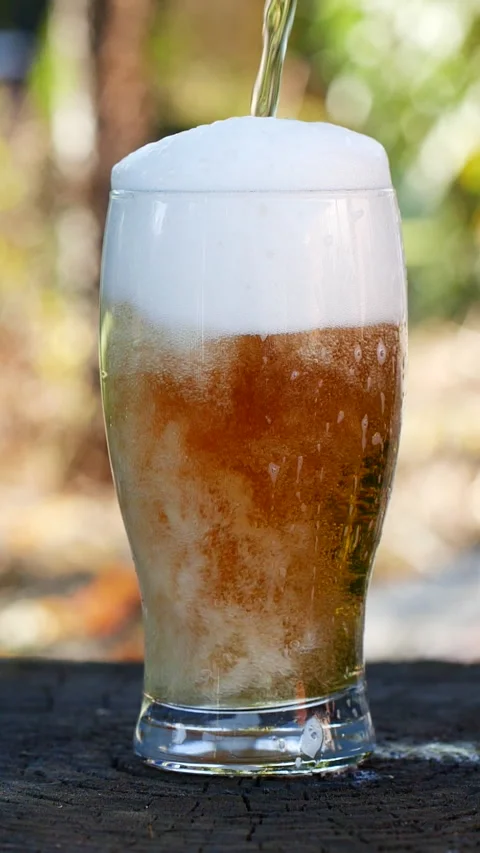 Vertical close-up of pouring beer with foam and bubbles in glass in slow motion Stock Footage 276525398
