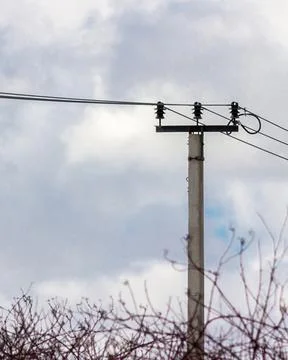 Vertical close-up of power line pole with overhead wires against cloudy sky Фото