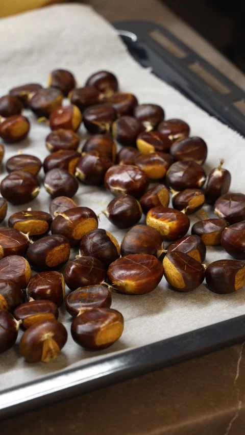 Vertical close-up of scored chestnuts arranged on parchment-lined baking tray Stock Footage 334179627