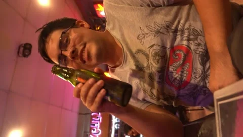 Vertical close-up shot of a man drinking beer from a glass bottle in a bar at ni Stock Footage 196737083