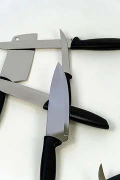 Vertical close-up shot of sharp kitchen knives placed on a white background Stock Photos