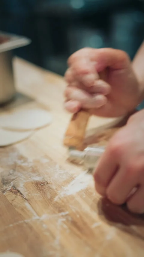 Vertical close-up of a small rolling pin rolling dumpling dough on floured board Stock-Footage 333897393