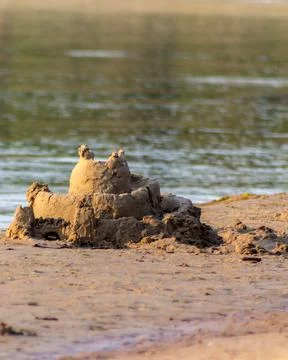 Vertical close-up of small sandcastle on sandy beach near calm water 写真素材