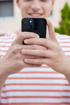Vertical close-up of smiling young man using smartphone app outdoors. Stock Photos