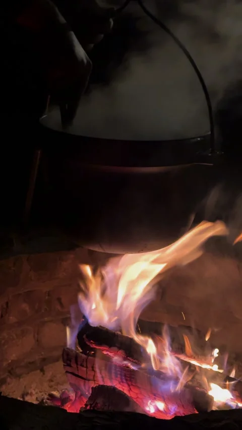 VERTICAL, CLOSE UP: Stirring steaming stew in a cast iron pot above firepit Stock Footage 341177069