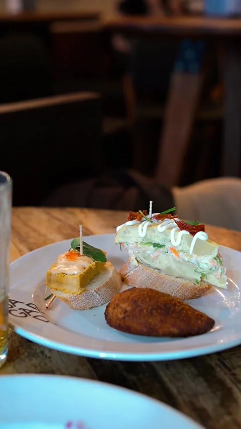 Vertical - Close-up of Traditional Spanish Appetizers in a Vibrant Bar Setting Stock Footage 329929351