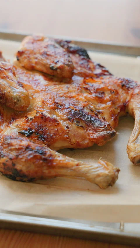 Vertical Close Up View of Crispy Spatchcock Roasted Chicken on a Baking Sheet wi Stock-Footage 338254660
