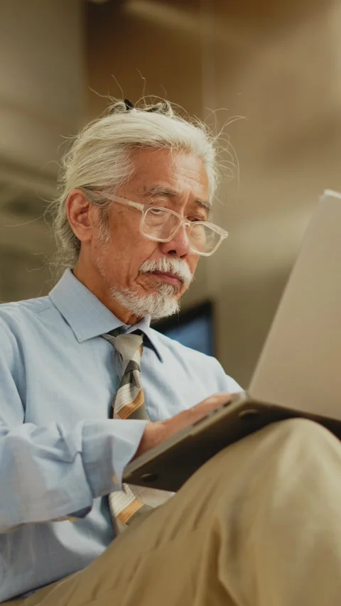 Vertical close view of senior Thai man reading screen and typing on laptop 動画素材 347776669