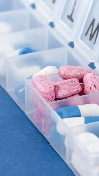 Vertical close up view of a white plastic daily pill container filled with pi Stock Photos