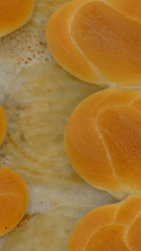 Vertical closeup of golden bread rolls on parchment-lined tray in bakery setting Stock Footage 344571703