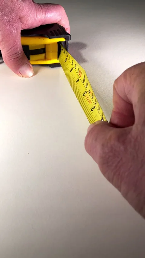 Vertical - Closeup of a man’s hands pulling a steel tape measure across a board. Video stock 282971055