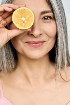 Vertical closeup portrait. Mid aged beautiful Asian woman holding juicy lemon. Stock Photos