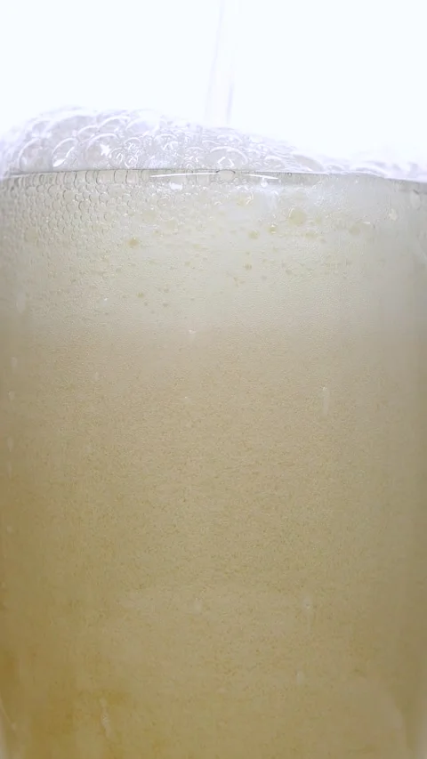 Vertical closeup of pouring beer with foam and bubbles in slow motion over white Stock Footage 265129409