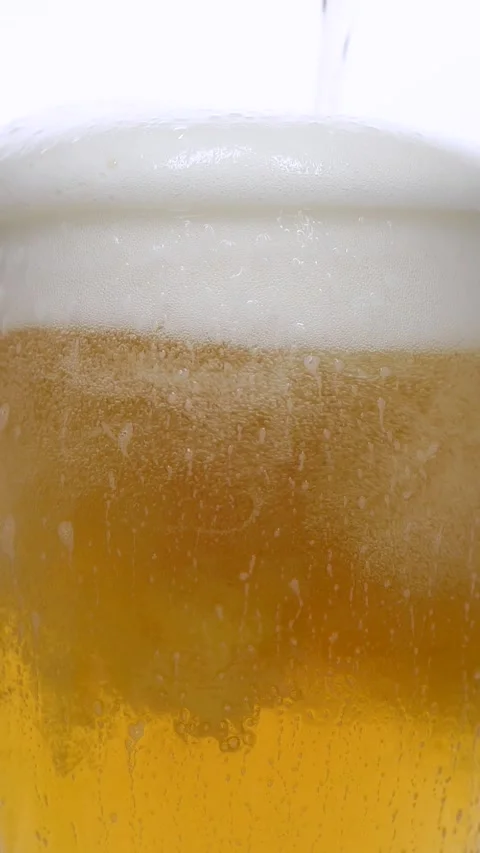 Vertical closeup of pouring beer with foam and bubbles in slow motion over white Stock Footage 265936700