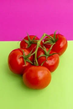 Vertical closeup shot of cherry tomatoes on a pink and green background Stock Photos