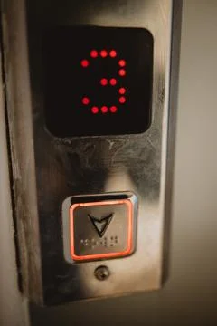 Vertical closeup shot of a pushed elevator button going down from the third floo Stock Photos
