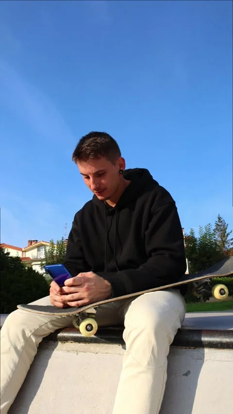 Vertical CloseUp of a Skater Texting on His Smartphone While Resting at the.. Stock Footage 285766228