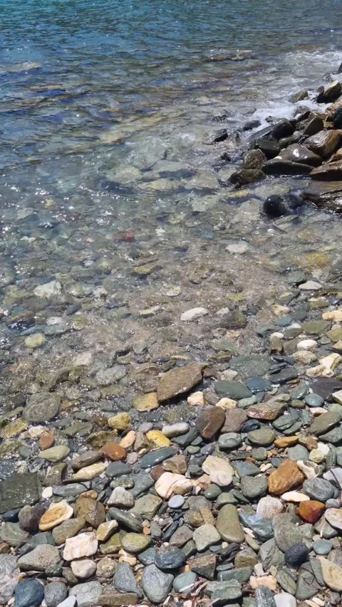 Vertical closeup view of colorful pebbles and crystal clear waves on the is.. Stock Footage 318216078
