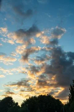 Vertical cloudscape of towering cumulus clouds glowing orange at sunset above Stock Photos