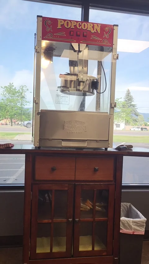 VERTICAL Commercial theater popcorn machine sits by window 스톡 동영상 339972482