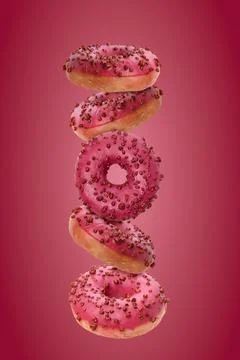 Vertical composition of levitating pink donuts with glaze and berry sprinkles Stock Photos