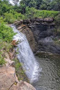 Vertical Composition Of Waterfall Cascading Down Rocky Cliff Face Into Stream Stock Photos