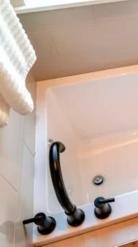 Vertical crop Rectangular bathtub with black faucet and handles against tile Foto stock