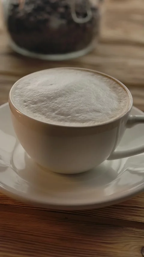 Vertical of A cup of coffee and a mobile phone on a wooden table in a cafe Stock Footage 276914613