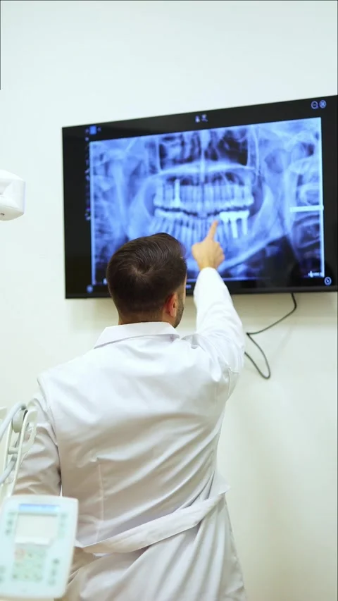 Vertical Dentist pointing at jaw x-ray explaining treatment to patient Stock Footage 295784526