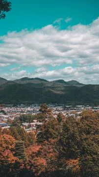 A vertical distant shot of a city surrounded by trees and mountains under a c Stock Photos