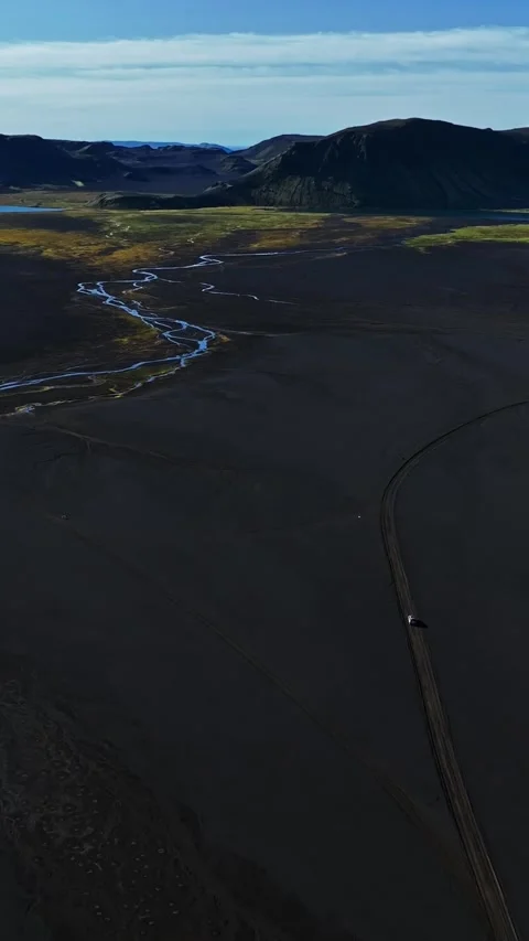 Vertical drone aerial of a tiny car driving a lonely track across a huge black 스톡 동영상 328337199