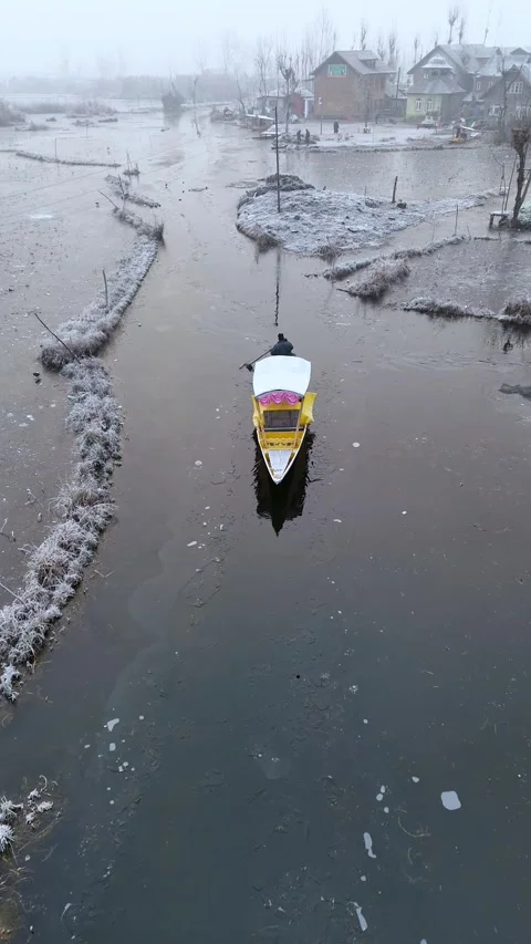 Vertical drone capturing a boatman chiseling through snow in Dal Lake’s frozen Stock Footage 311019478