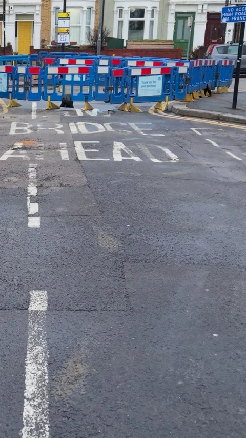 Vertical drone flight over road in London past signs and tarmac hole Stock Footage 328558313