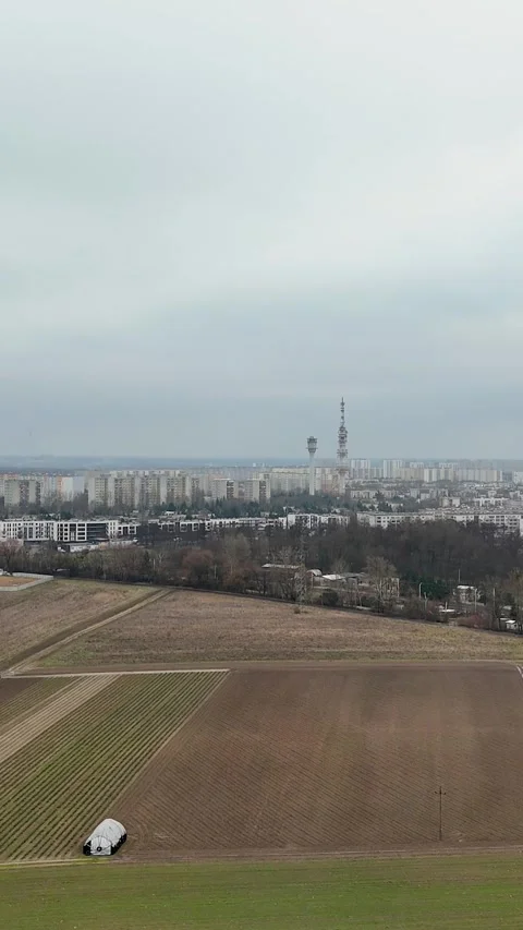 Vertical Drone Flying Forward Over Bare Field Toward Distant City Skyline Stock Footage 330751286