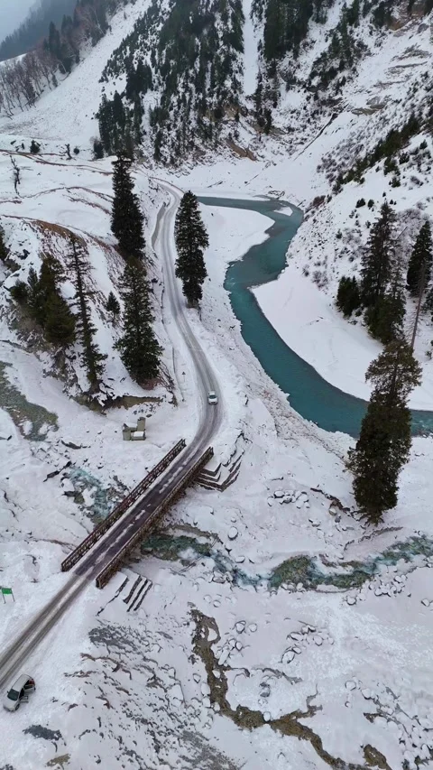 Vertical Drone flying over a serene winter valley with a frozen road, sparkling Stock Footage 311019479